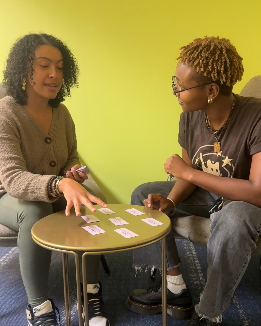 A wellness coach giving instructions on an activity to a student participant, while pointing at cards on a table.