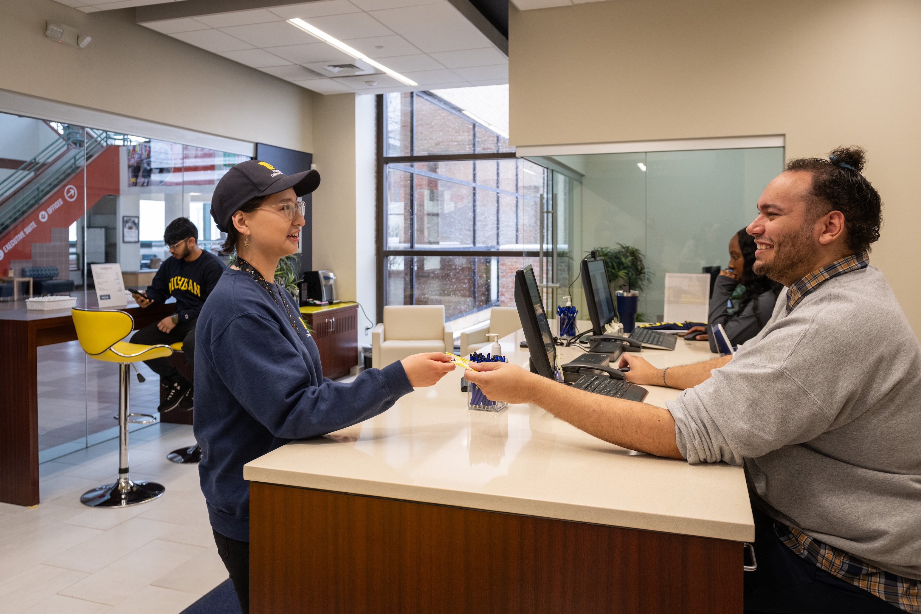 University of Michigan staff assisting a student at a service desk in a campus building.