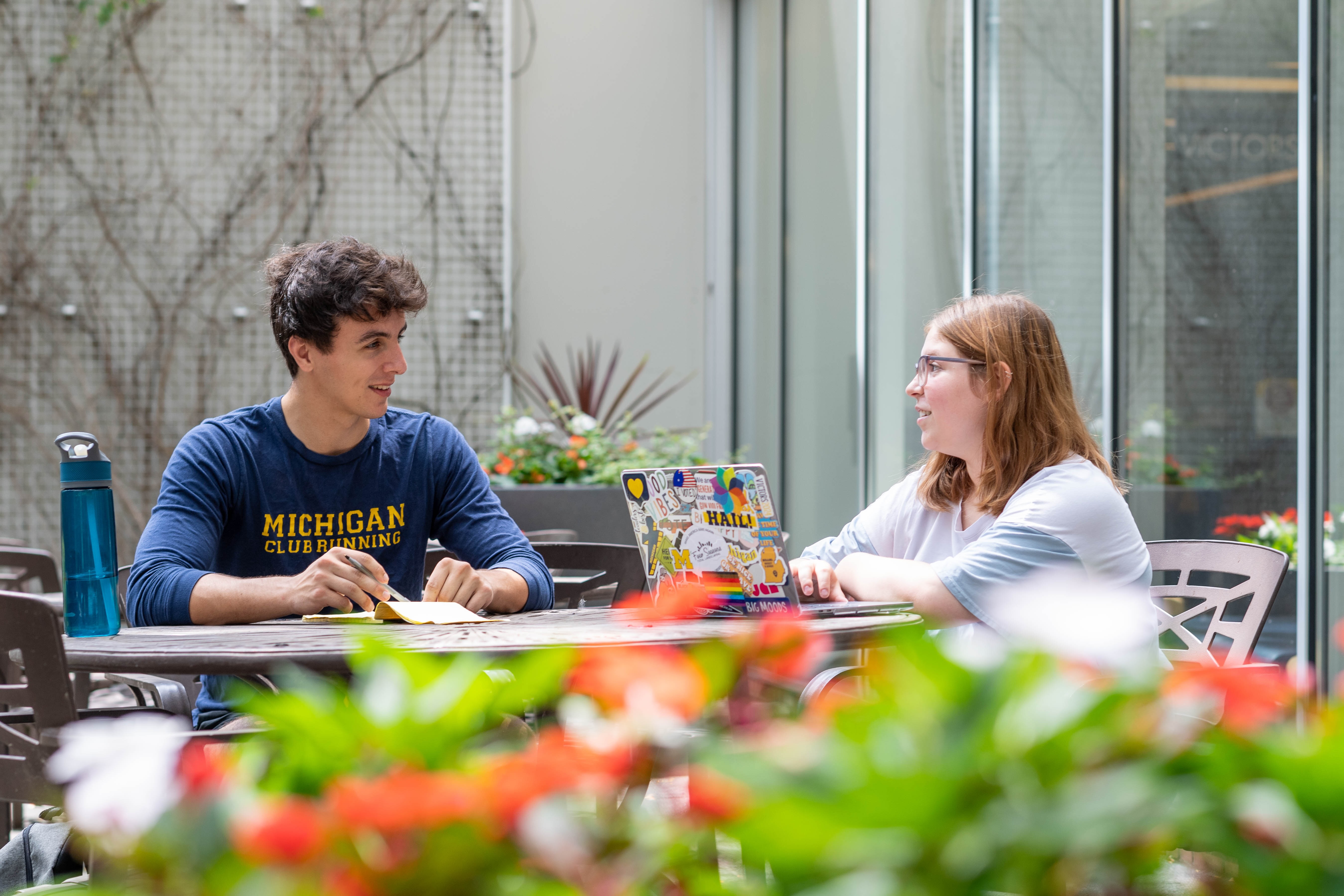 Two students sitting at an outdoor table having a conversation.