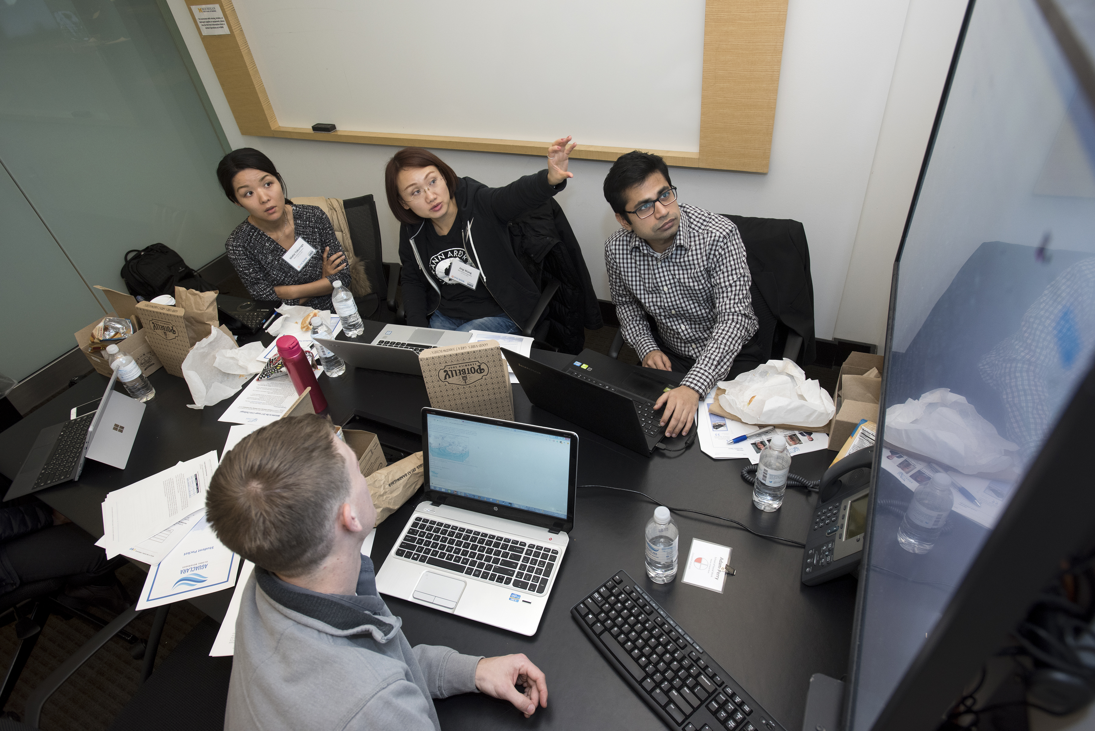 Students with laptops planning together in a study room by looking at a screen.