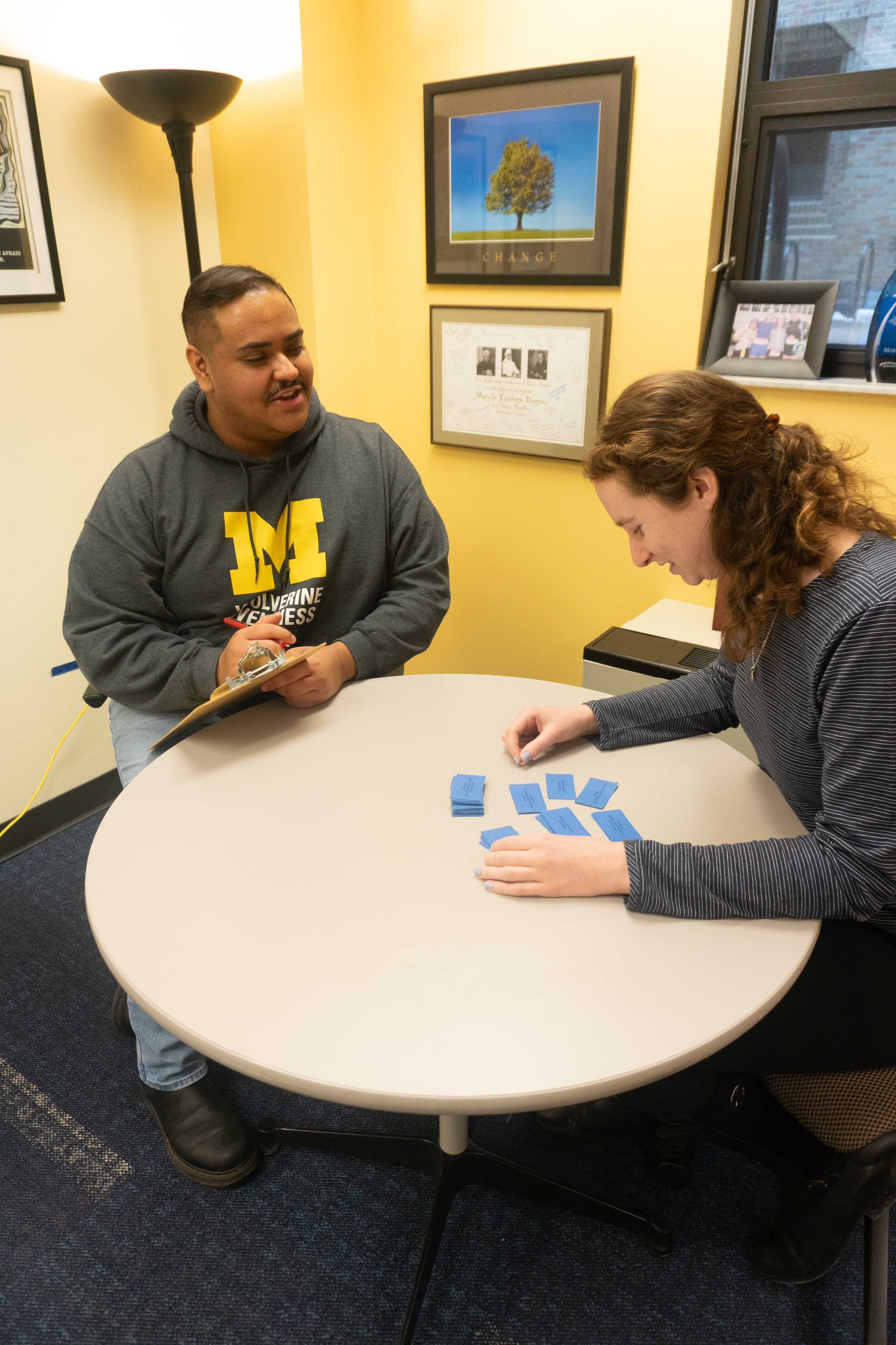 A student participant sorting cards on a table while a wellness coach observes and takes notes.