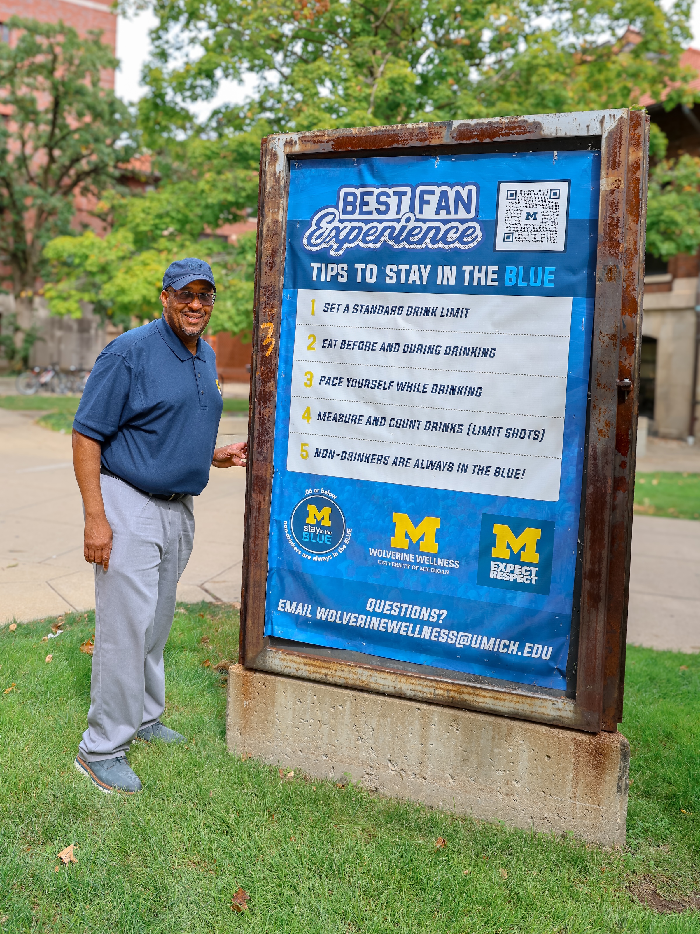 U-M's VP for Student Life poses with a Diag board promoting our Best Fan Experience, which gives tips to Stay in the Blue.