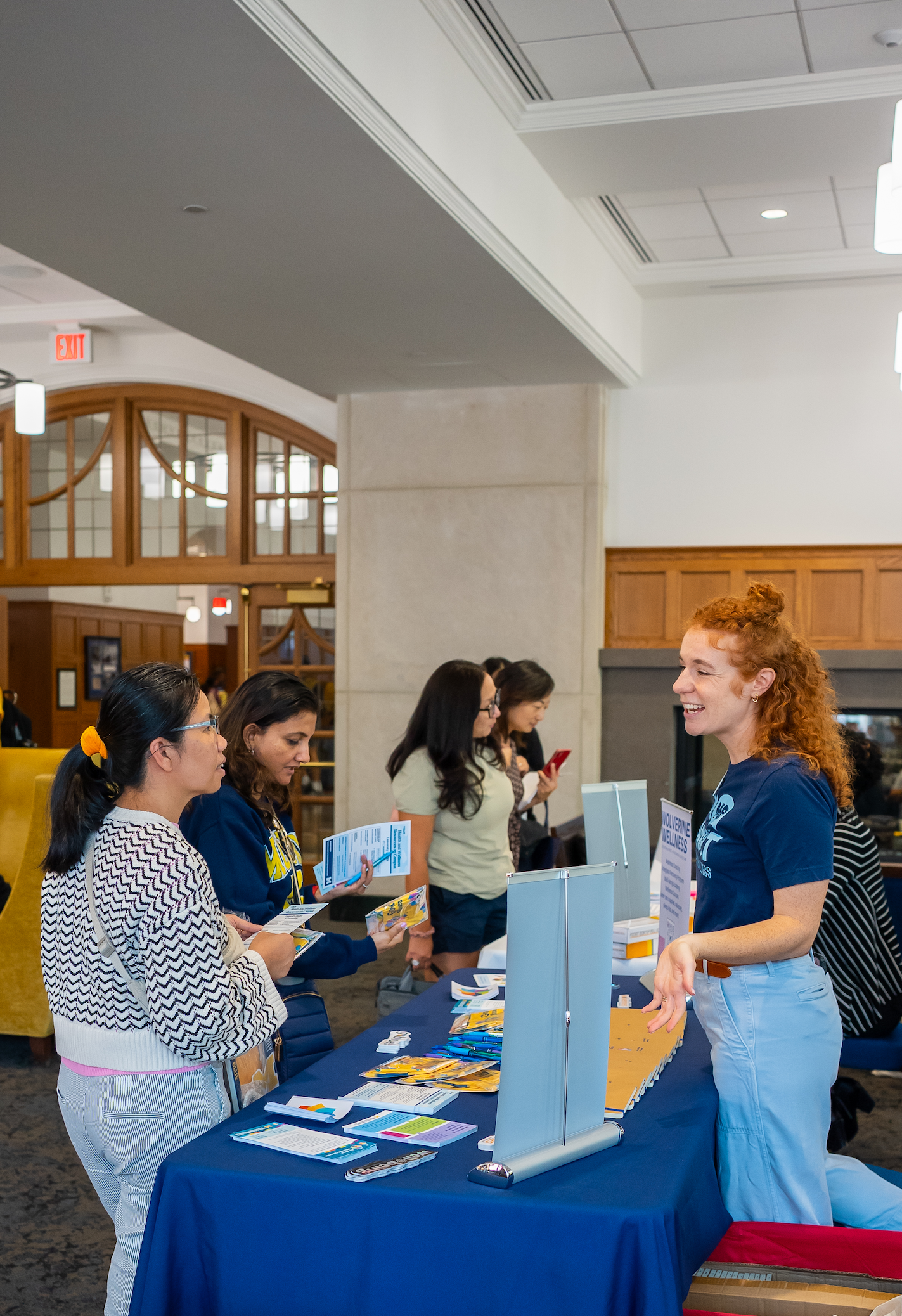 A Wolverine Wellness staff member talks with attendees at an information table filled with brochures in the Michigan Union lobby during Parent-Family weekend.  the